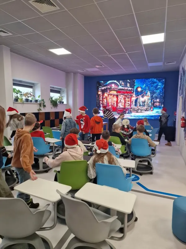 Dzieci w czapkach Mikołaja siedzą w Pracowni przed ekranem – 