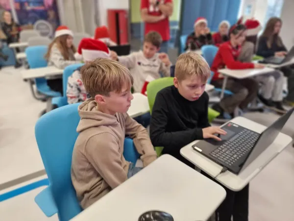 Dzieci w czapkach Mikołaja siedzą w Pracowni przy komputerach – 