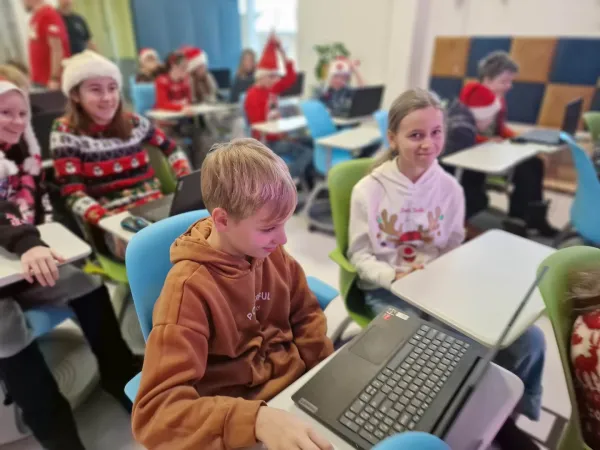 Dzieci w czapkach Mikołaja siedzą w Pracowni przy komputerach – 